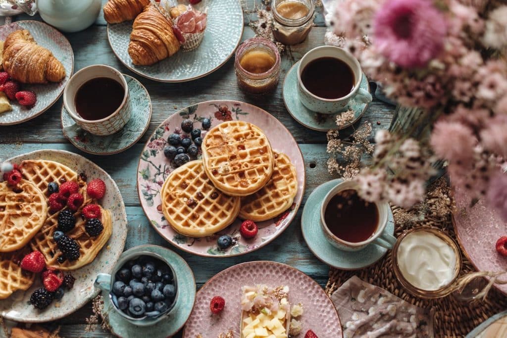 brunch gourmand avec viennoiseries, pancakes et jus d’orange après une nuit blanche vue dessus pancake gauffre thé café table fruit rouge framboise croissants