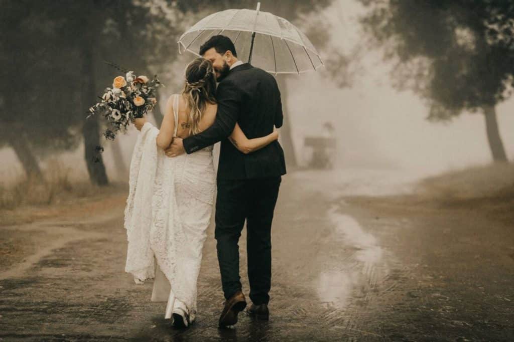 mariés marche long d'un chemin parapluie transparent pluie robe mariage trempée