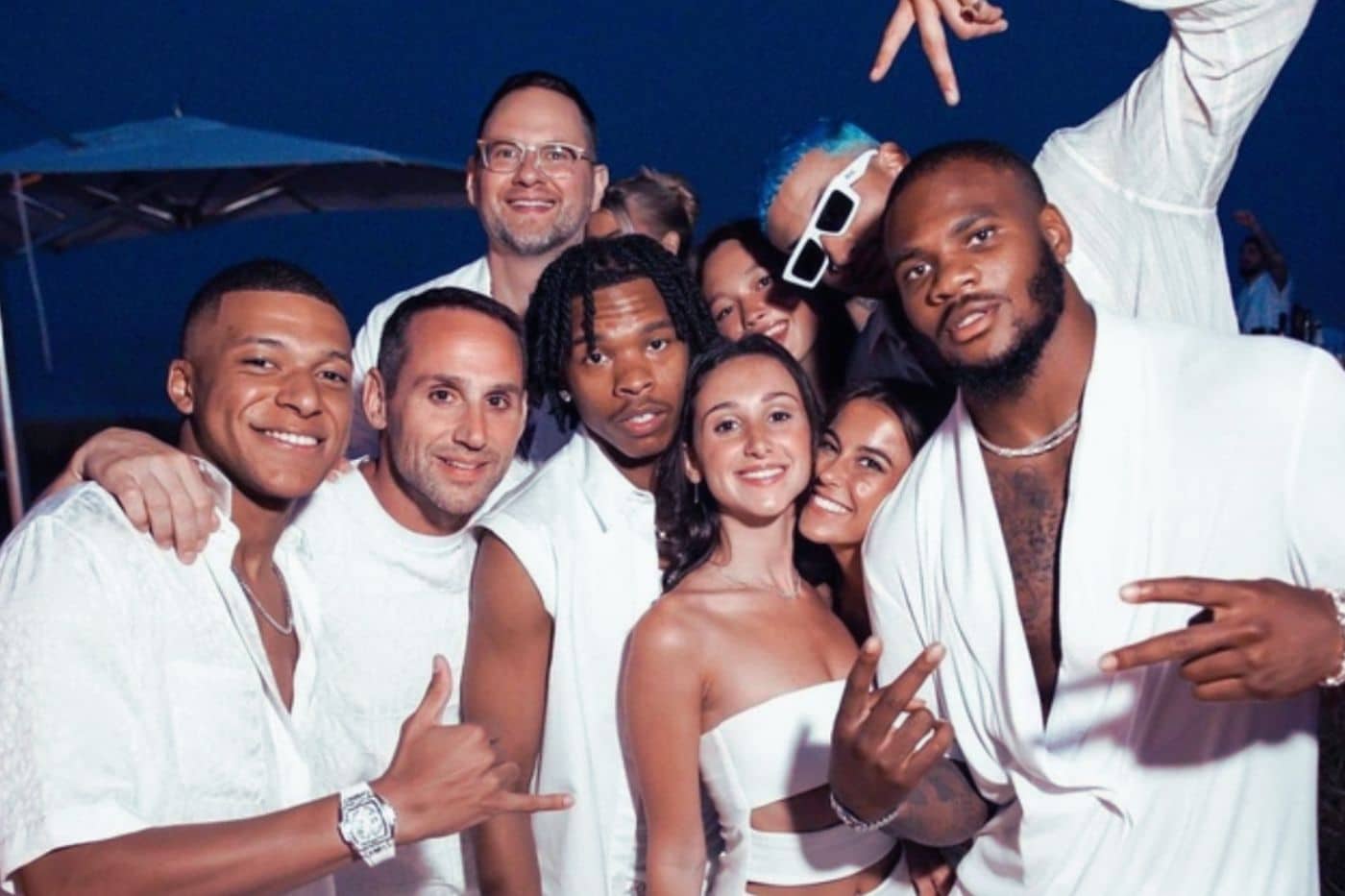Invités habillés en blanc réunis autour d’une longue table en extérieur, sous des guirlandes lumineuses, lors d’une soirée blanche élégante et festive white party mbappe michael rubin