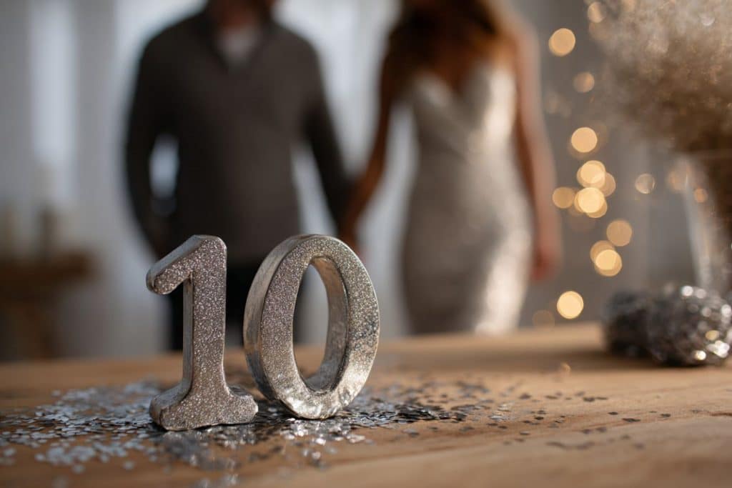 noces d’étain pour 10 ans de mariage avec chiffre 10 en étain et ambiance argentée couple amoureux se tenant par la main dans le fond flouté