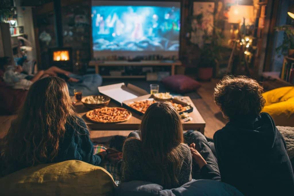 Adolescents de 14 ans regardant un film ensemble dans un salon cocooning avec pizza et pop-corn
