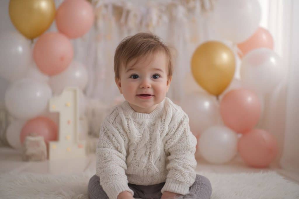 bébé 1 an assis et riant entouré de ballons pastel rose or